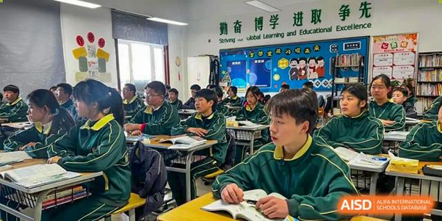Students in green and yellow uniforms seated at desks listening to a lesson in a classroom at Maple Leaf International School-Zhenjiang.