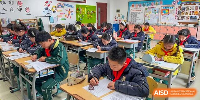 A male student concentrating on his writing or test at his desk in a classroom at Maple Leaf International School-Zhenjiang.