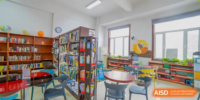 The interior of a small, bright library or reading nook with bookshelves, tables, and chairs at Maple Leaf International School-Zhenjiang.
