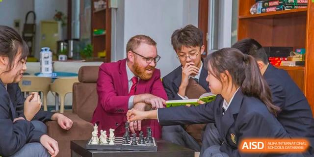 A teacher with a beard wearing a red suit playing chess with a male student in a dark suit at Maple Leaf International School-Zhenjiang.