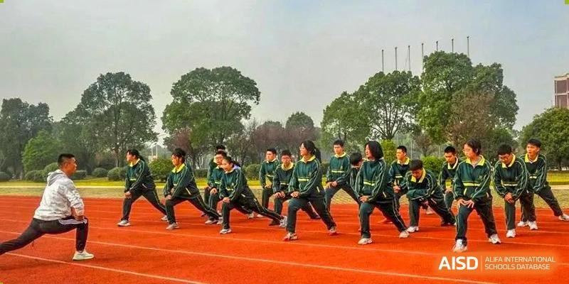 A group of students in green uniforms performing warm-up lunges on a red running track outdoors at Maple Leaf International School-Zhenjiang.