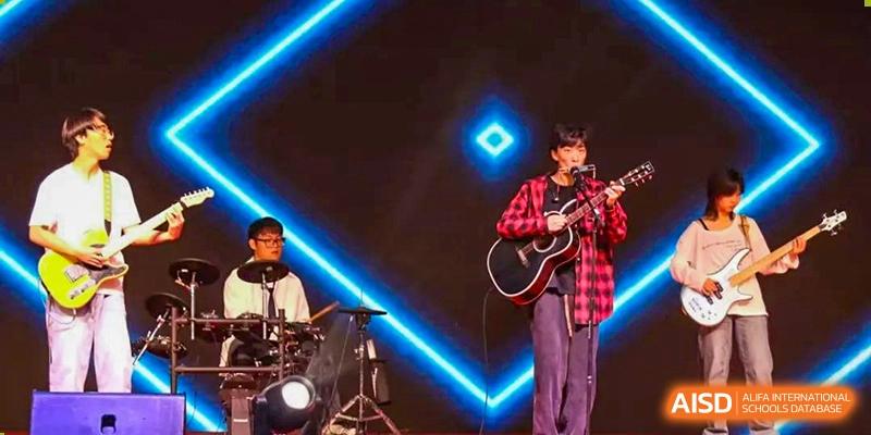 A student performing an electric guitar solo on a brightly lit stage with neon accents at Maple Leaf International School-Zhenjiang.