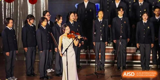 A female student in a white gown playing the violin as part of a musical ensemble on stage at Maple Leaf International School-Zhenjiang.