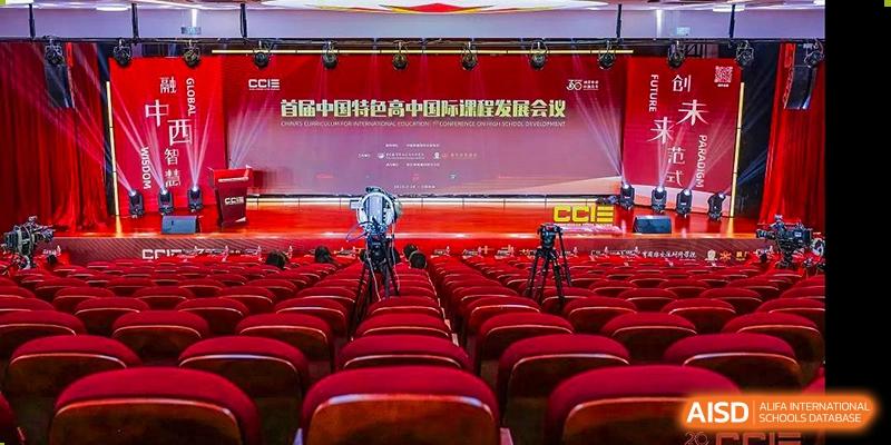 A wide-angle view of a large, modern auditorium with rows of empty red seats and a stage banner at Maple Leaf International School-Zhenjiang.