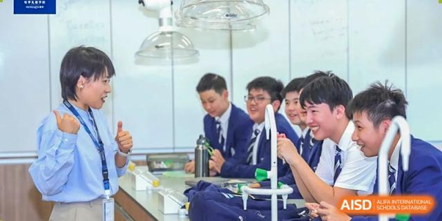 High school students from Harrow LiDe School Hengqin in uniform conduct a science experiment in a lab, working with glassware and equipment.