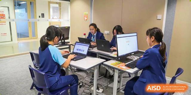 Students from Harrow LiDe School Hengqin work collaboratively on their laptops at tables in a bright, modern learning area.