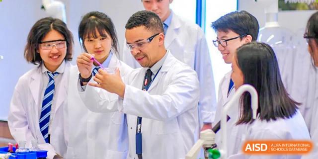 A science teacher or instructor in a lab coat at Harrow LiDe School Hengqin guides students on an experiment, holding up a specimen.