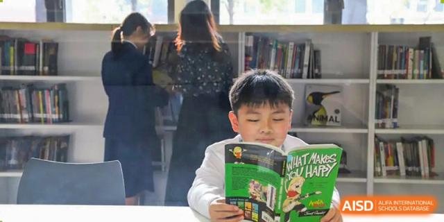 A young male student from Harrow LiDe School Hengqin sits and reads a book in the school library.