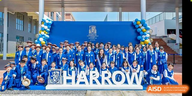 A large group of students from Harrow LiDe School Hengqin in blue uniforms poses for a group photo in front of the large "HARROW" sign.