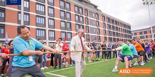 Head of School, in a white suit, participates in a tug-of-war competition with students on the outdoor pitch at Harrow LiDe School Hengqin.