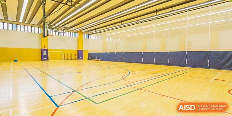 Interior wide view of the well-lit, empty indoor sports hall and wooden floor with court markings at Harrow LiDe School Hengqin.