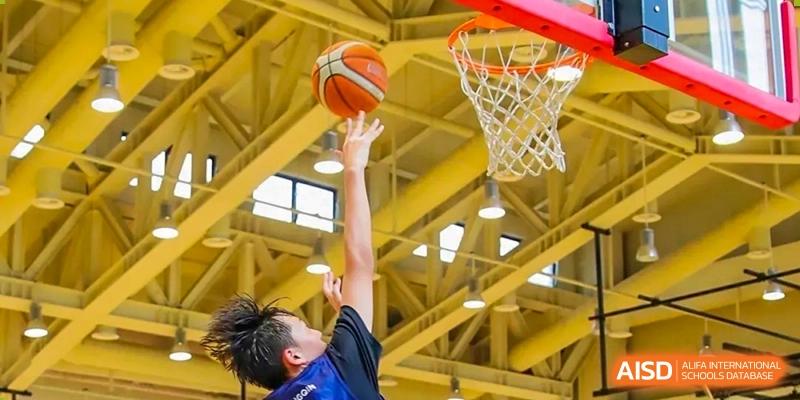 A student from Harrow LiDe School Hengqin jumps up to shoot a basketball into the hoop in the bright indoor gymnasium.