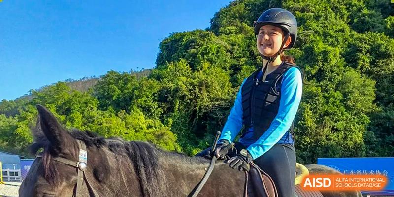 A student from Harrow LiDe School Hengqin rides a horse outdoors in a scenic, mountainous natural environment.