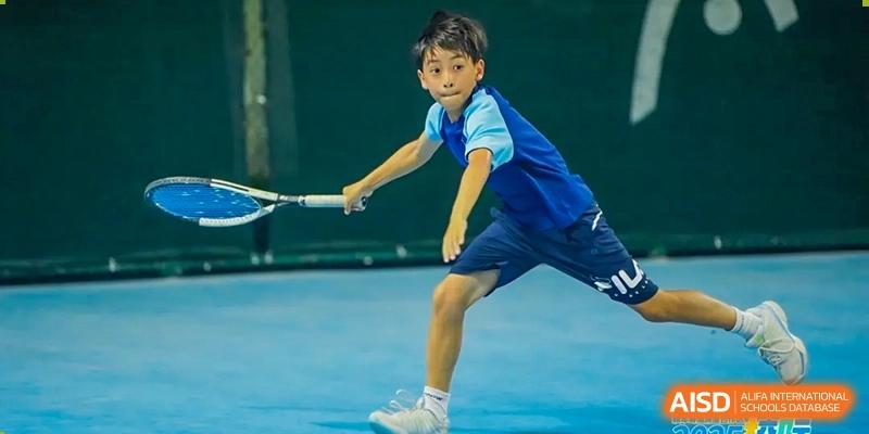 A young male student from Harrow LiDe School Hengqin plays tennis or badminton, reaching out to hit a ball with his racket.