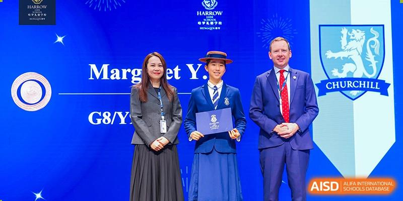 A female student from Harrow LiDe School Hengqin in uniform receives an award on stage from a staff member.