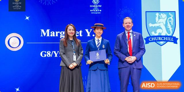 A female student from Harrow LiDe School Hengqin in uniform receives an award on stage from a staff member.