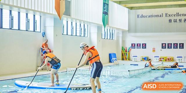 A student from Harrow LiDe School Hengqin practices kayaking or water safety skills in the indoor pool with a paddle.