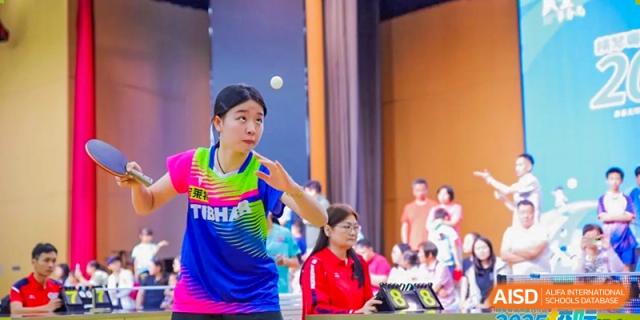 A female student from Harrow LiDe School Hengqin plays table tennis, focusing on the ball during a rally.