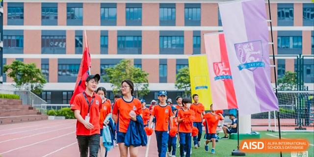 A large group of students from Harrow LiDe School Hengqin wearing matching orange shirts walks outdoors during a school event.