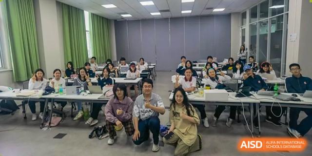 A group of students posing for a photo, with some seated at desks and others kneeling in the front at the High School Affiliated to Shanghai Jiao Tong University.