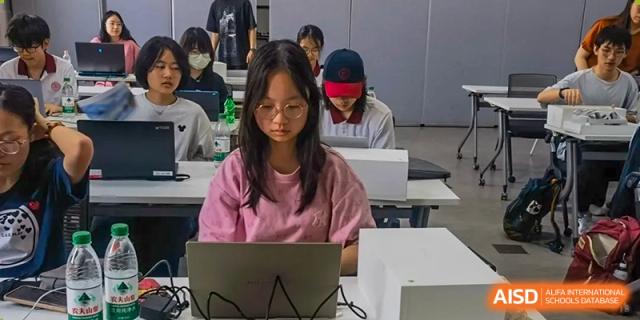 A female student wearing a pink shirt using a laptop in a classroom or study hall at the High School Affiliated to Shanghai Jiao Tong University.