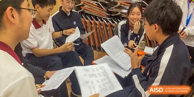 A group of students in uniform reviewing and discussing papers in a classroom at the High School Affiliated to Shanghai Jiao Tong University.