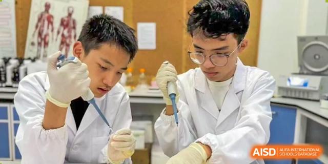 Two students in lab coats and gloves working with beakers and pipettes in a science lab at the High School Affiliated to Shanghai Jiao Tong University.