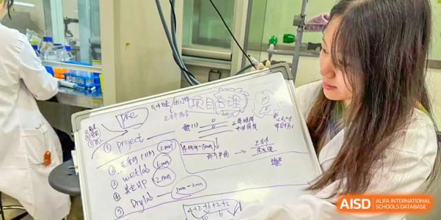A hand holding a small whiteboard with handwritten chemical equations and scientific notes at the High School Affiliated to Shanghai Jiao Tong University.