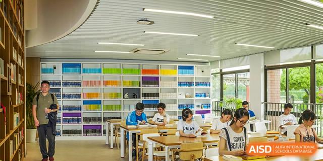 Students working at tables in a brightly colored library with bookshelves in the background at the High School Affiliated to Shanghai Jiao Tong University.