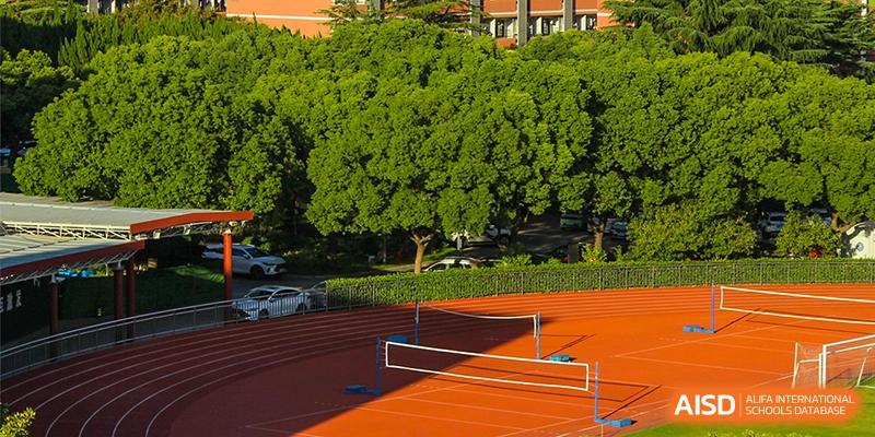 An outdoor sports complex with a volleyball net, running track, and a large tree at the High School Affiliated to Shanghai Jiao Tong University.