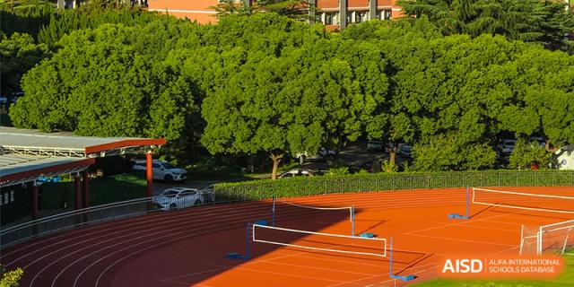 An outdoor sports complex with a volleyball net, running track, and a large tree at the High School Affiliated to Shanghai Jiao Tong University.