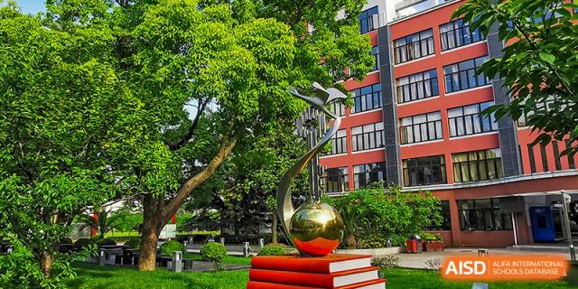 A sculpture of a golden sphere on top of red books in a landscaped area at the High School Affiliated to Shanghai Jiao Tong University.