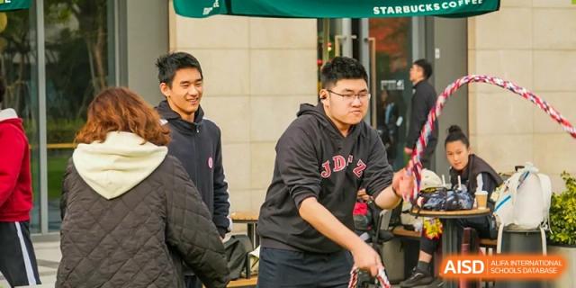 Students sitting at tables in a relaxed setting, with one student looking at the camera and another in the background at the High School Affiliated to Shanghai Jiao Tong University.