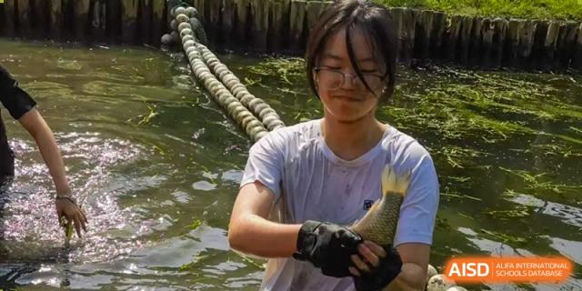 A student holding a small fish while participating in an outdoor activity at the High School Affiliated to Shanghai Jiao Tong University.