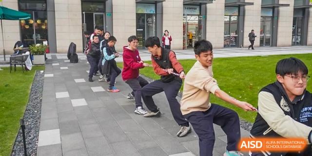 Students participating in a tug-of-war game on a paved area outside at the High School Affiliated to Shanghai Jiao Tong University.