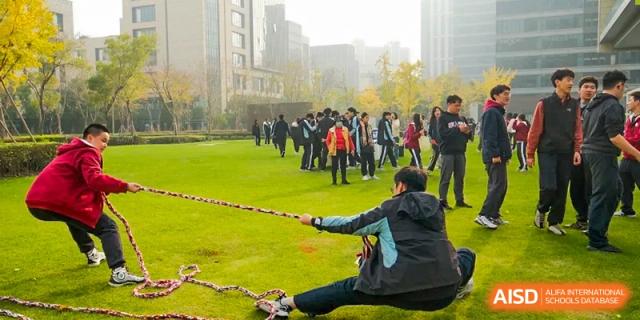 A group of students playing a tug-of-war game on a grassy field at the High School Affiliated to Shanghai Jiao Tong University.