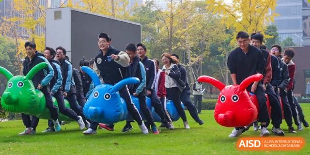 Students participating in an inflatable racing game on a grassy field at the High School Affiliated to Shanghai Jiao Tong University.