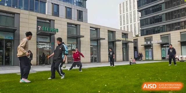 A student in a red sweatshirt playing a game on the grass while other students watch in the background at the High School Affiliated to Shanghai Jiao Tong University.