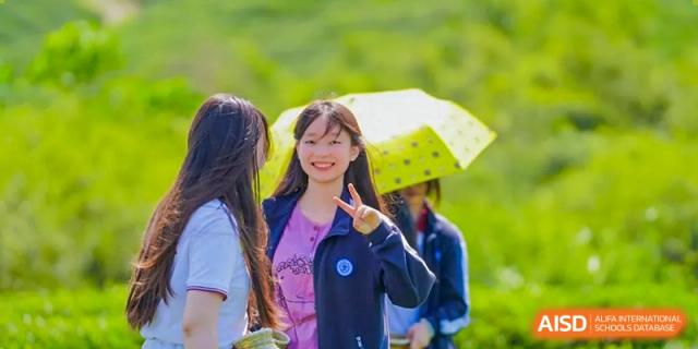 A smiling female student making a peace sign gesture while holding a green umbrella at the High School Affiliated to Shanghai Jiao Tong University.