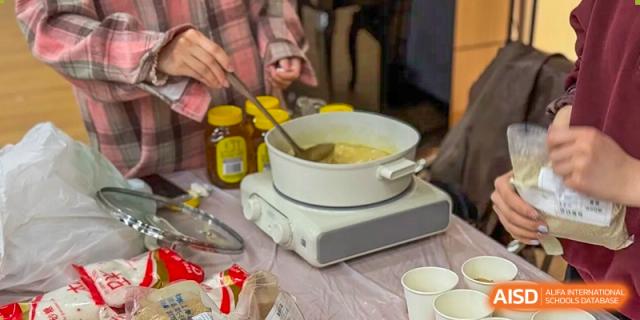 A close-up of a pot on a portable stove, with a hand stirring a thick mixture at the High School Affiliated to Shanghai Jiao Tong University.