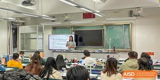 A teacher lecturing to students in a modern classroom with a large display screen at the Guangdong Overseas Chinese High School International Curriculum.