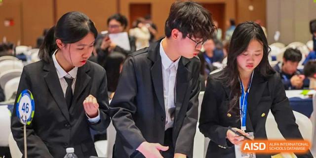 A student in a black suit, likely from the Guangdong Overseas Chinese High School International Curriculum, walking in a group indoors.