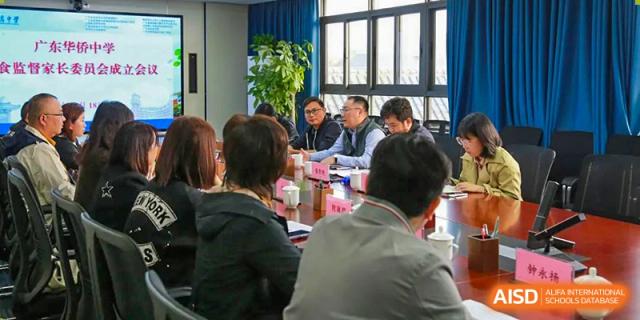 A group of teachers or staff at the Guangdong Overseas Chinese High School International Curriculum gathered for an indoor meeting or discussion.