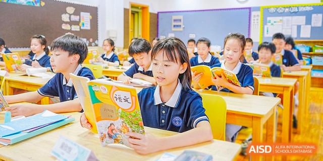 A student from Wahaha Bilingual School Hangzhou is smiling and holding a book in a classroom.