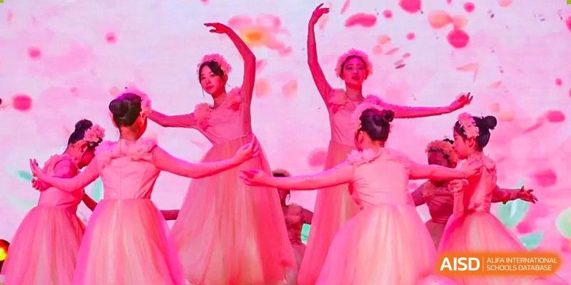 Female students from Wahaha Bilingual School Hangzhou are performing a graceful dance on a stage with a pink background.