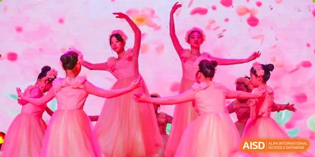 Female students from Wahaha Bilingual School Hangzhou are performing a graceful dance on a stage with a pink background.