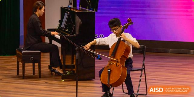 A male student at Wahaha Bilingual School Hangzhou is playing a cello during a performance.
