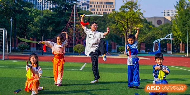 A male student at Wahaha Bilingual School Hangzhou is performing a martial arts pose with a sword on a sports field.