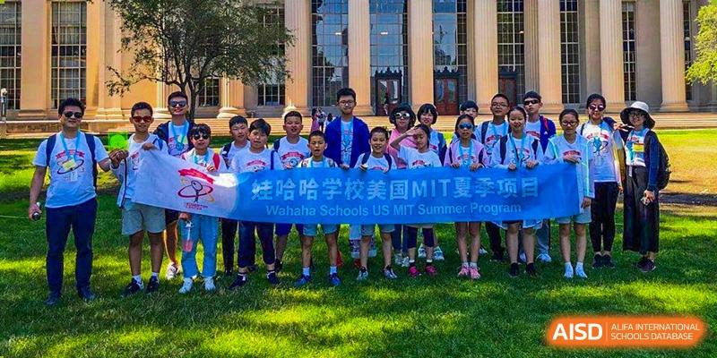 A group of students from Wahaha Bilingual School Hangzhou are posing for a photo, holding a blue banner that says 'MIT.'
