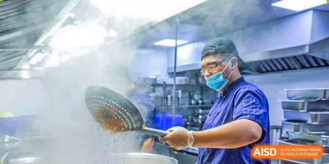 A chef is working in the kitchen at Wahaha Bilingual School Hangzhou, stirring a large pot.